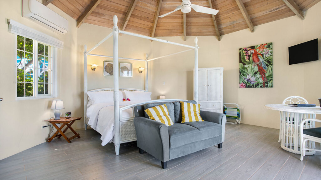 Arawak_suite-10-3_1600 Bright bedroom with colorful pillows, armchair, and ceiling fan in the Starfish Suite at Arawak Beach Club in Anguilla