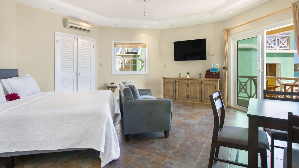 Arawak_suite-6-1_1600 Suite interior with bed, dining table, and TV in Ocean Bliss Suite at Arawak Beach Club in Anguilla