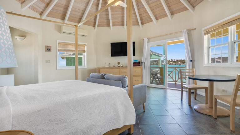 King bed with vaulted ceiling, sofa, and TV in the Sunset Suite at Arawak Beach Club in Anguilla